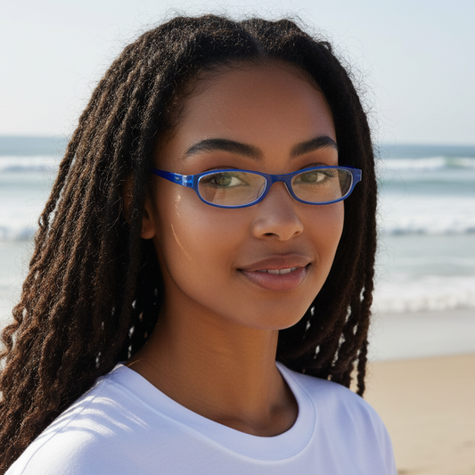 A woman wearing Mellow Monkey blue pocket reading glasses on a sunny beach with the ocean in the background.