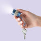 Mellow Monkey blue keychain flashlight with rhinestones and carabiner, held by a hand with white nails.