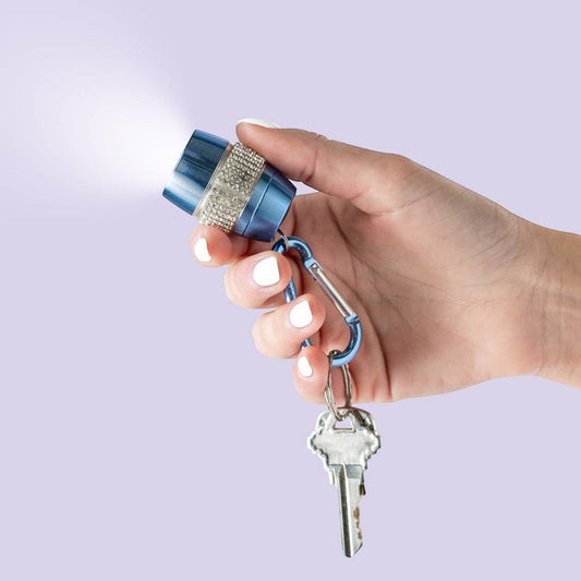 Mellow Monkey blue keychain flashlight with rhinestones and carabiner, held by a hand with white nails.