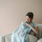 Mellow Monkey Bluebell nursing cover in soft light blue organic cotton muslin with a built-in silicone teether.