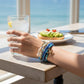 Mellow Monkey blue beaded bracelet set with seashell and starfish charms worn by a woman at a beachside cafe.