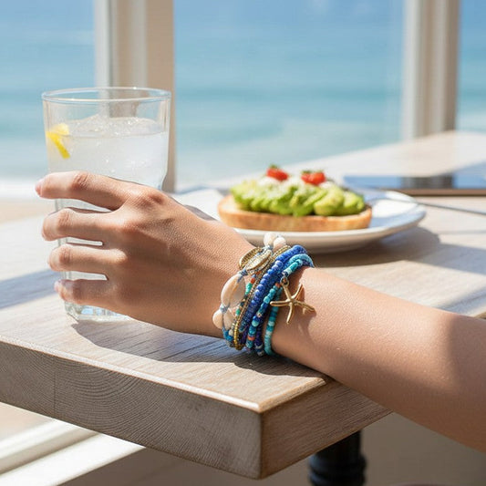 Mellow Monkey blue beaded bracelet set with seashell and starfish charms worn by a woman at a beachside cafe.