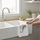 Mellow Monkey white cotton flour sack towel with a colorful boho mermaid illustration hanging on a farmhouse sink.