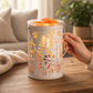 Mellow Monkey Botanical Glow fragrance warmer with cream metal floral cutouts and glowing wax melt on wooden table
