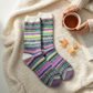 Mellow Monkey Nordic crew socks with a colorful botanical fair isle pattern on a cozy cream knit blanket with tea.
