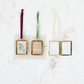 Mellow Monkey brass and glass photo frame ornaments with red, green, and white velvet ribbon hangers on white surface