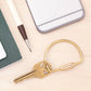 Mellow Monkey brass keyring with a secure screw-in clasp on a light wooden surface with a pen and phone