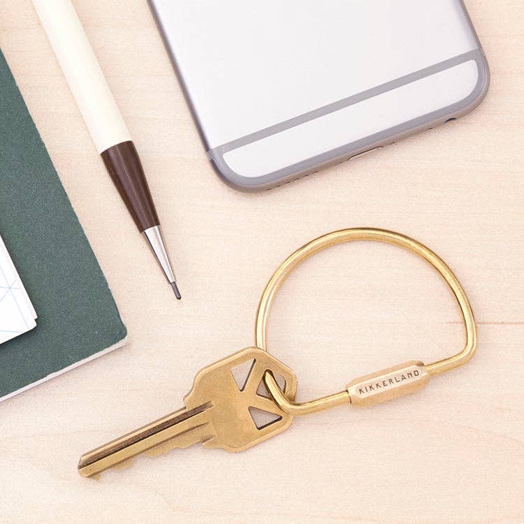 Mellow Monkey brass keyring with a secure screw-in clasp on a light wooden surface with a pen and phone