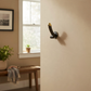 Mellow Monkey 6-inch antique brass wall hook with a unique phallic design and dark patina finish on a beige wall.