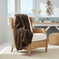 Mellow Monkey brown faux fur throw blanket draped over a wicker armchair in a coastal living room setting