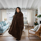 Woman wrapped in a plush brown faux fur throw blanket from Mellow Monkey in a bright, coastal-style living room.