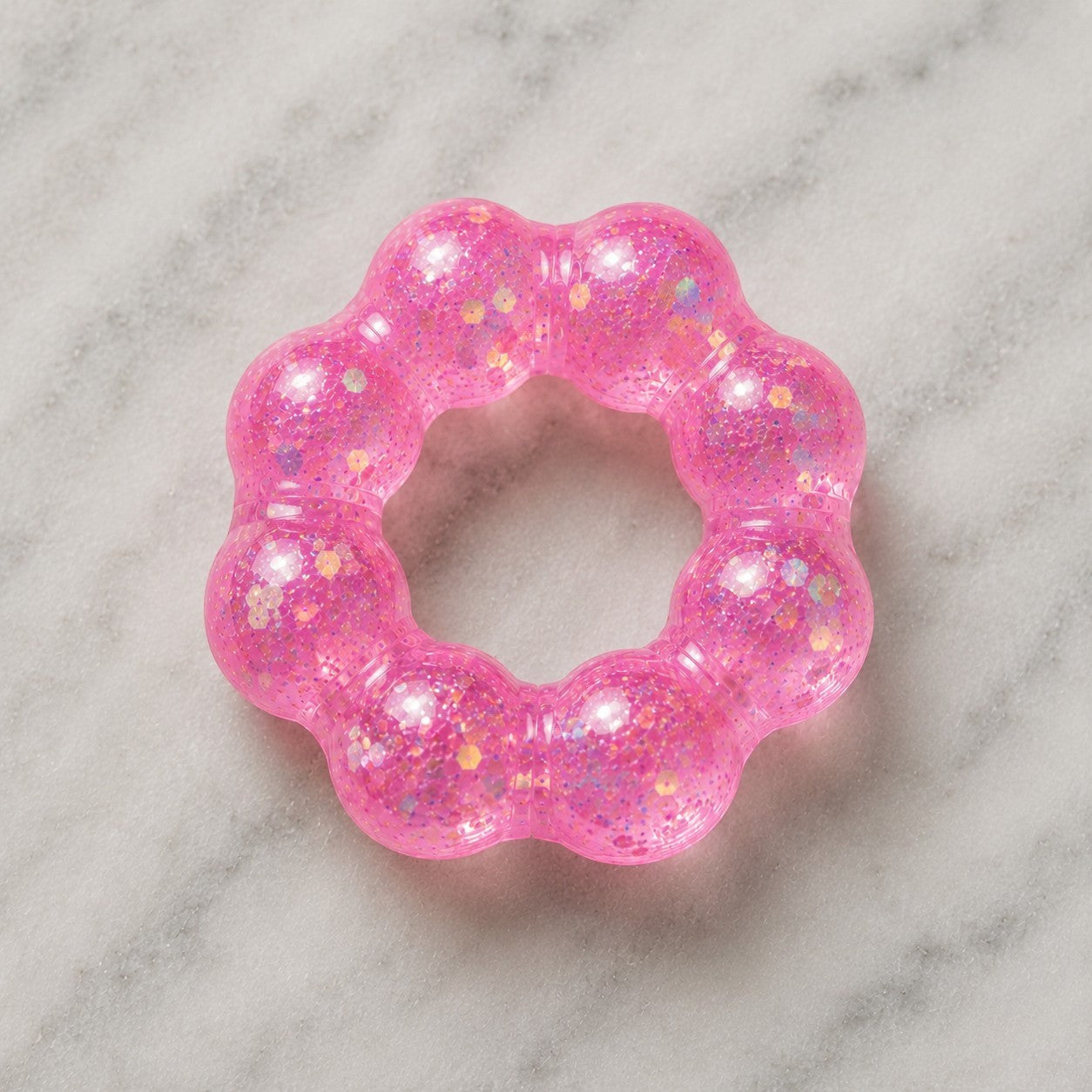 Mellow Monkey Bubblegum Glow Feelzies sensory bracelet in translucent pink with glitter on a marble surface.