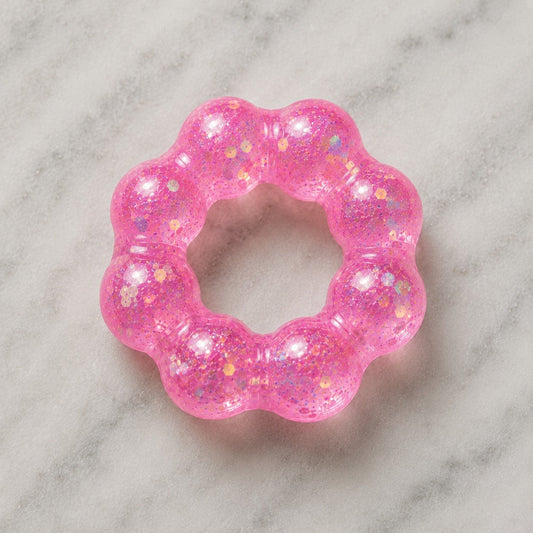 Mellow Monkey Bubblegum Glow Feelzies sensory bracelet in translucent pink with glitter on a marble surface.