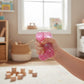 Mellow Monkey Bubblegum Glow Feelzies sensory bracelet being squeezed by a child in a bright playroom.