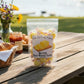 Mellow Monkey Butter Salt Water Taffy, individually wrapped yellow candies in a clear bag, on a picnic table with croissants and coffee.