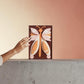 Mellow Monkey Together Tile Acrylic Wall Art, 5x7-in, featuring a butterfly design in pink, orange, and white with a brown background.