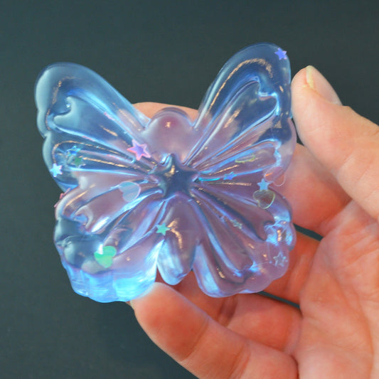 Mellow Monkey butterfly-shaped jelly squishy in translucent blue with glittery star and heart accents held in hand