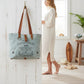 Mellow Monkey La Couspaude canvas tote bag with brown leather handles hanging on a white rustic wall