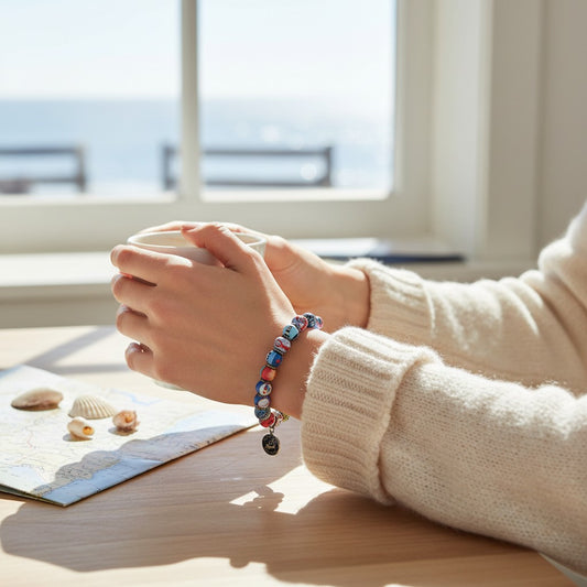 Mellow Monkey Cape Cod bracelet with hand-painted nautical clay beads worn by a person holding a mug by the sea.