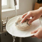 Mellow Monkey Moki cat dish scrubber, taupe with black embroidered face, used for washing a plate.