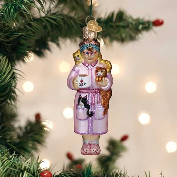 Mellow Monkey Cat Lady glass ornament with cats, holding a mug that says CATS. Pink robe, slippers, glasses.