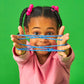 Young girl playing with Mellow Monkey Cat's Cradle blue cotton string game against a bright green background