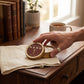 Mellow Monkey Wood Aromatics cedar wood hand salve in a round tin held by a hand on a wooden desk with books and tea.