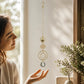 Mellow Monkey celestial eye suncatcher with gold chains and hanging crystal prism held by a woman near a window