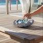 Mellow Monkey large dusty blue ceramic shell bowl filled with glass spheres on a wooden table by the beach.