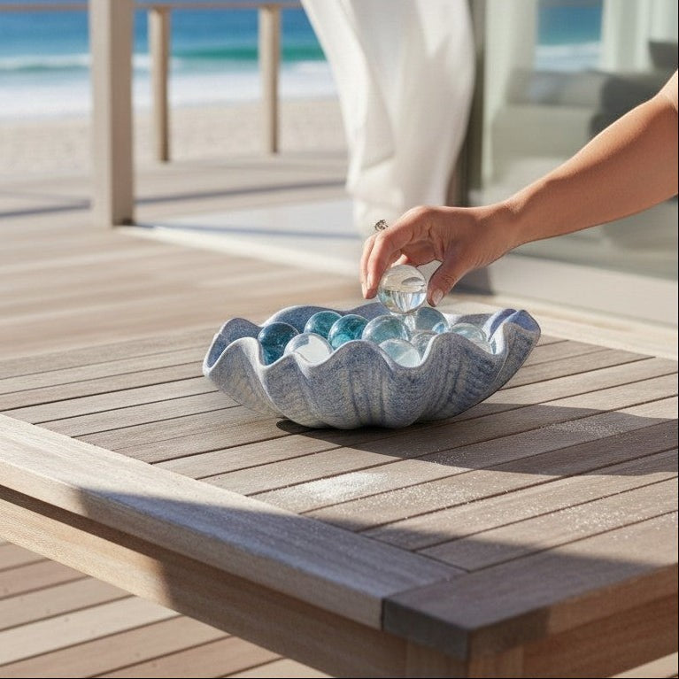 Mellow Monkey large dusty blue ceramic shell bowl filled with glass spheres on a wooden table by the beach.