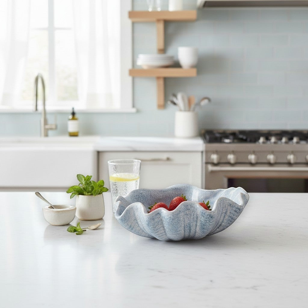 Mellow Monkey large ceramic shell bowl in dusty blue with reactive glaze, displayed on a kitchen counter with fruit.