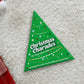 Mellow Monkey Christmas Charades game in a green tree-shaped box on a white rug with festive decorations.