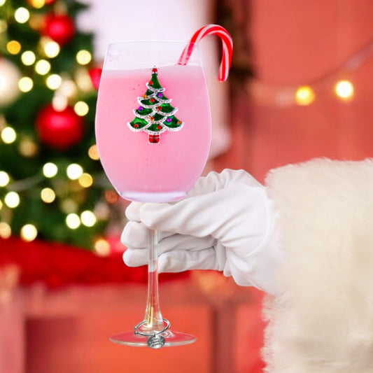 Mellow Monkey stemmed wine glass featuring a jeweled Christmas tree design, held by a hand in a white Santa glove.