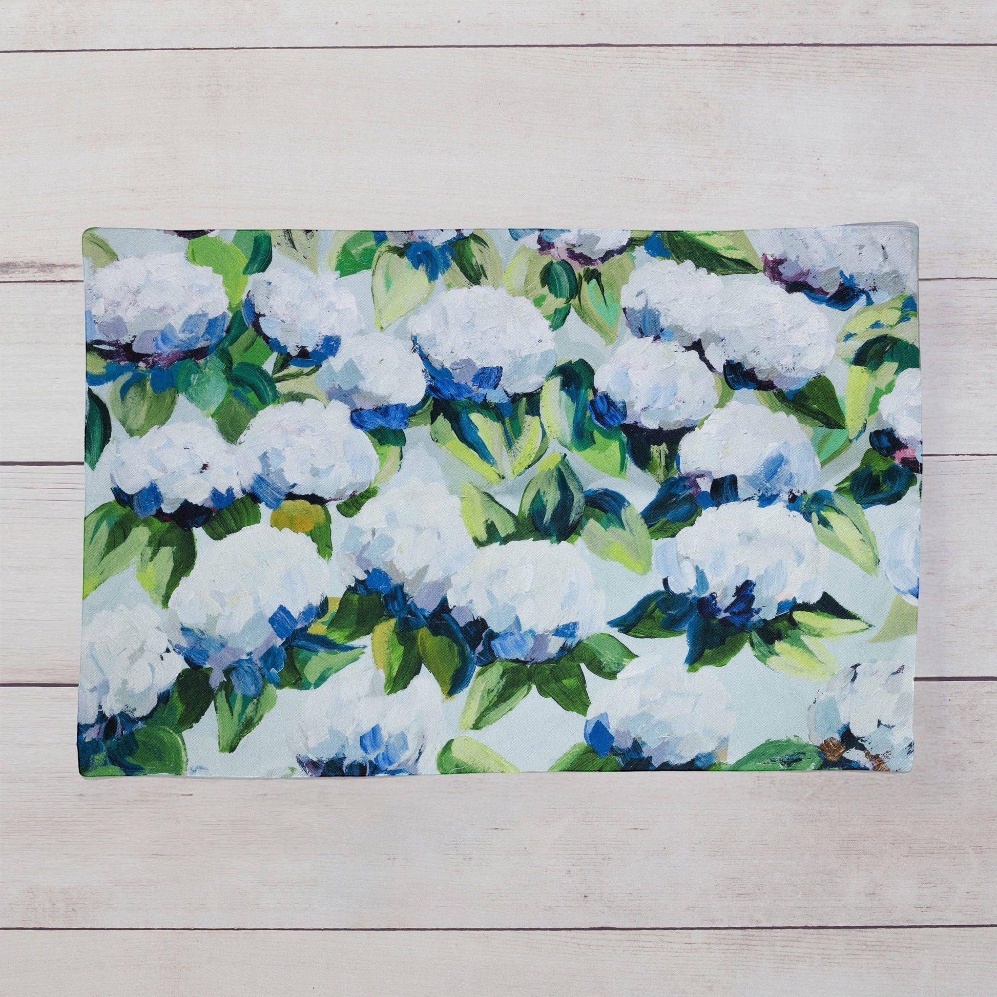 Mellow Monkey Coastal Hydrangea reversible woven cotton placemat with blue and white floral art on a wood table.