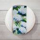 Mellow Monkey cotton dinner napkin featuring a coastal hydrangea floral print in blue, white, and green on a plate.