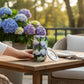 Mellow Monkey 16oz stainless steel wine tumbler with a blue and purple coastal hydrangea floral print on a patio table