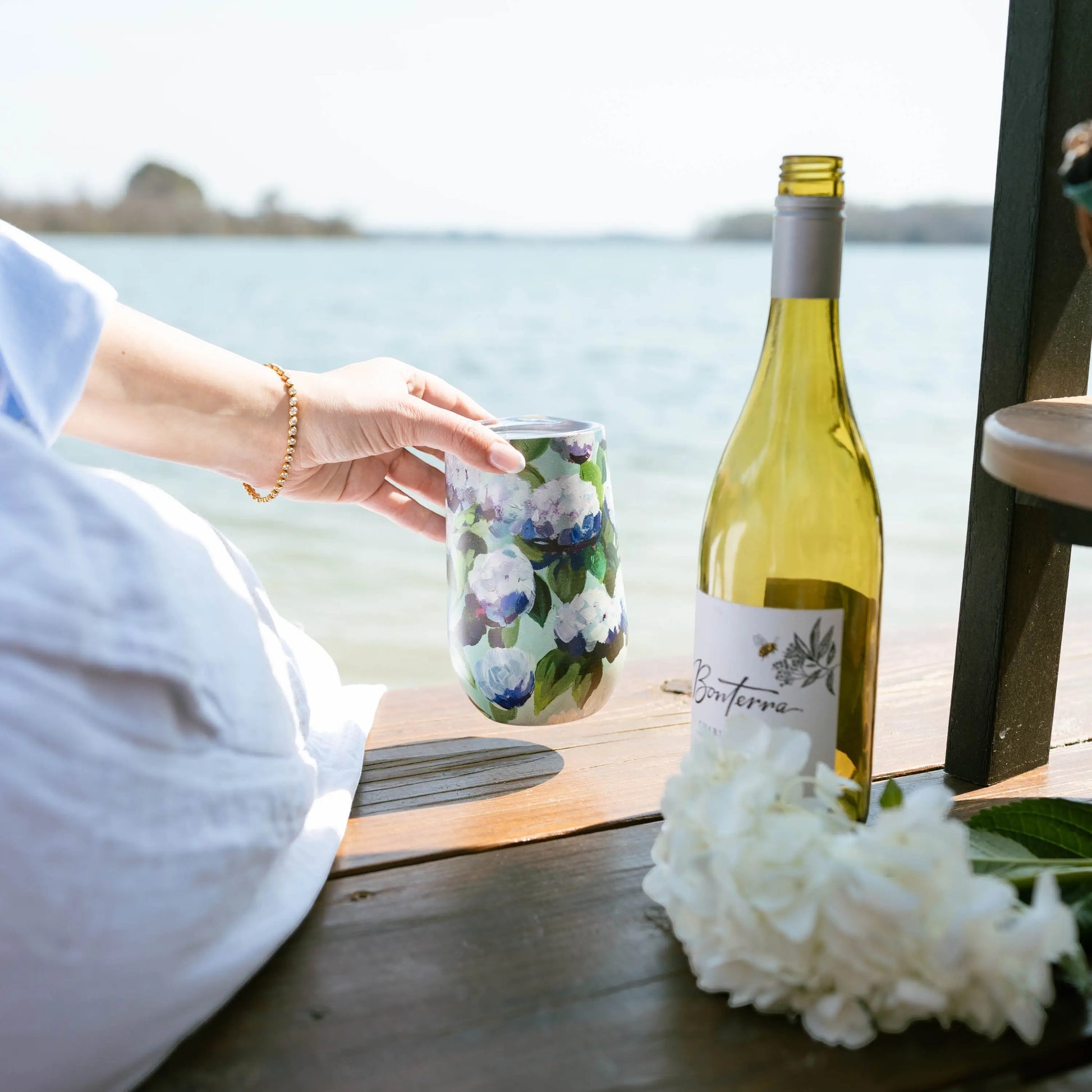 Mellow Monkey 16oz stainless steel wine tumbler with a blue and white coastal hydrangea floral print on a dock.
