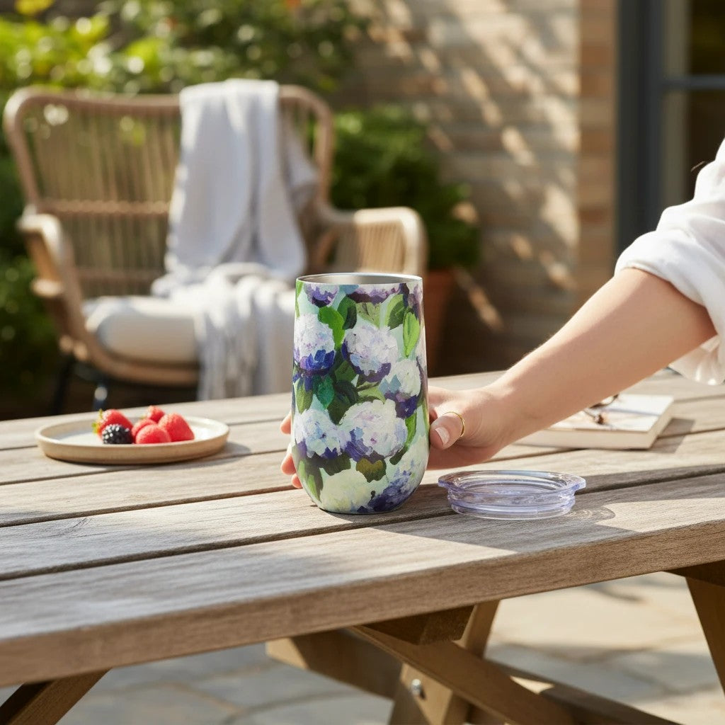 Mellow Monkey 16oz stainless steel wine tumbler with a blue and purple coastal hydrangea floral print on a patio table
