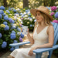 Woman in a straw hat holding a Mellow Monkey 12oz insulated mug with coastal art in a garden of blue hydrangeas.