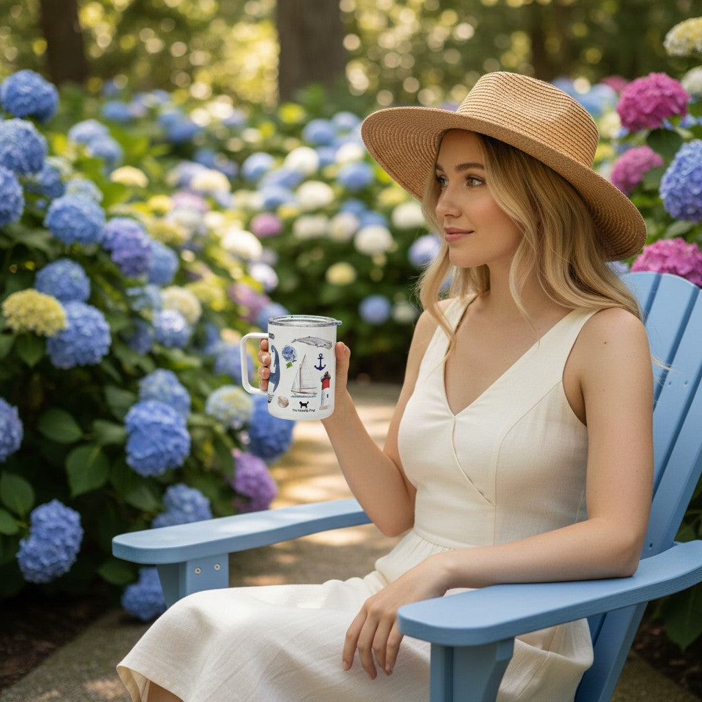 Woman in a straw hat holding a Mellow Monkey 12oz insulated mug with coastal art in a garden of blue hydrangeas.