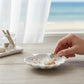 Mellow Monkey coastal trio earrings featuring gold starfish, shells, and pearls in a white ceramic shell dish.