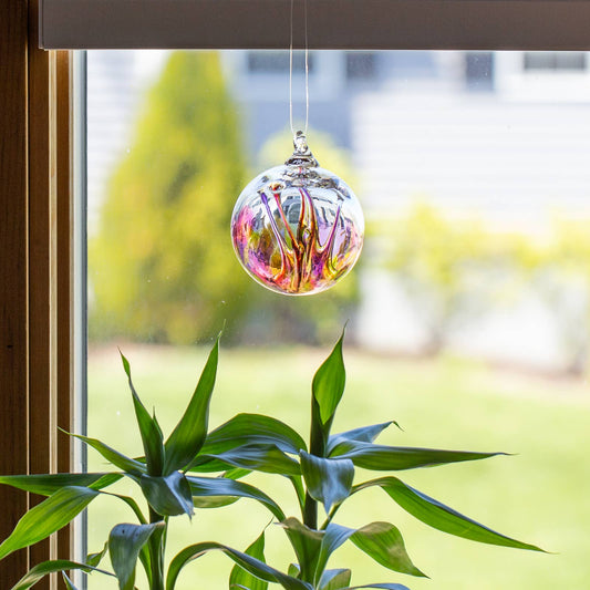 Mellow Monkey 3-inch colorful glass wish ornament hanging in a window above a green plant