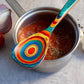 Mellow Monkey Montego Bay colorful wooden cooking spoon with teal, blue, red, orange, and yellow swirls. 12.5-in.