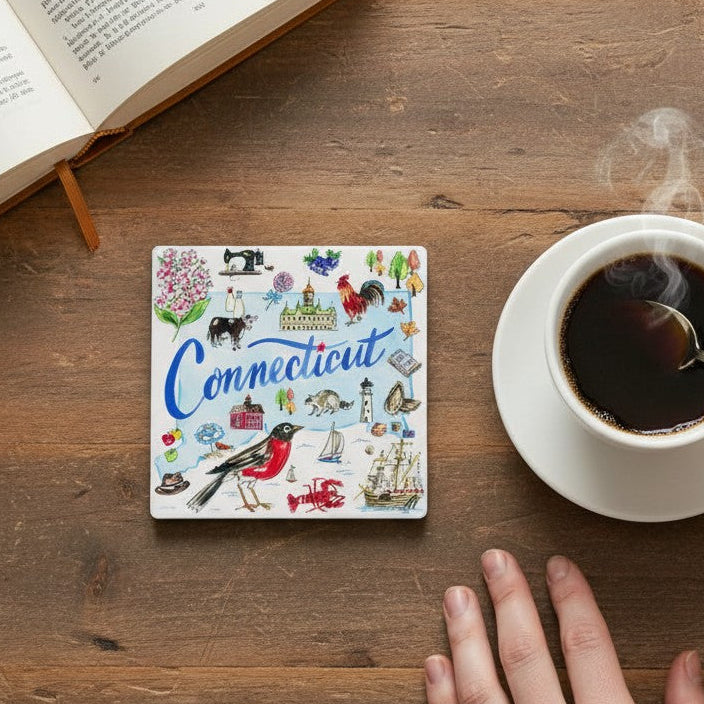 Mellow Monkey ceramic Connecticut state coaster with colorful illustrated icons on a rustic wooden table with coffee.