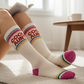 Mellow Monkey Cool Aunt gym crew socks in white with pink and teal stripes, worn by a woman reading on a rug.