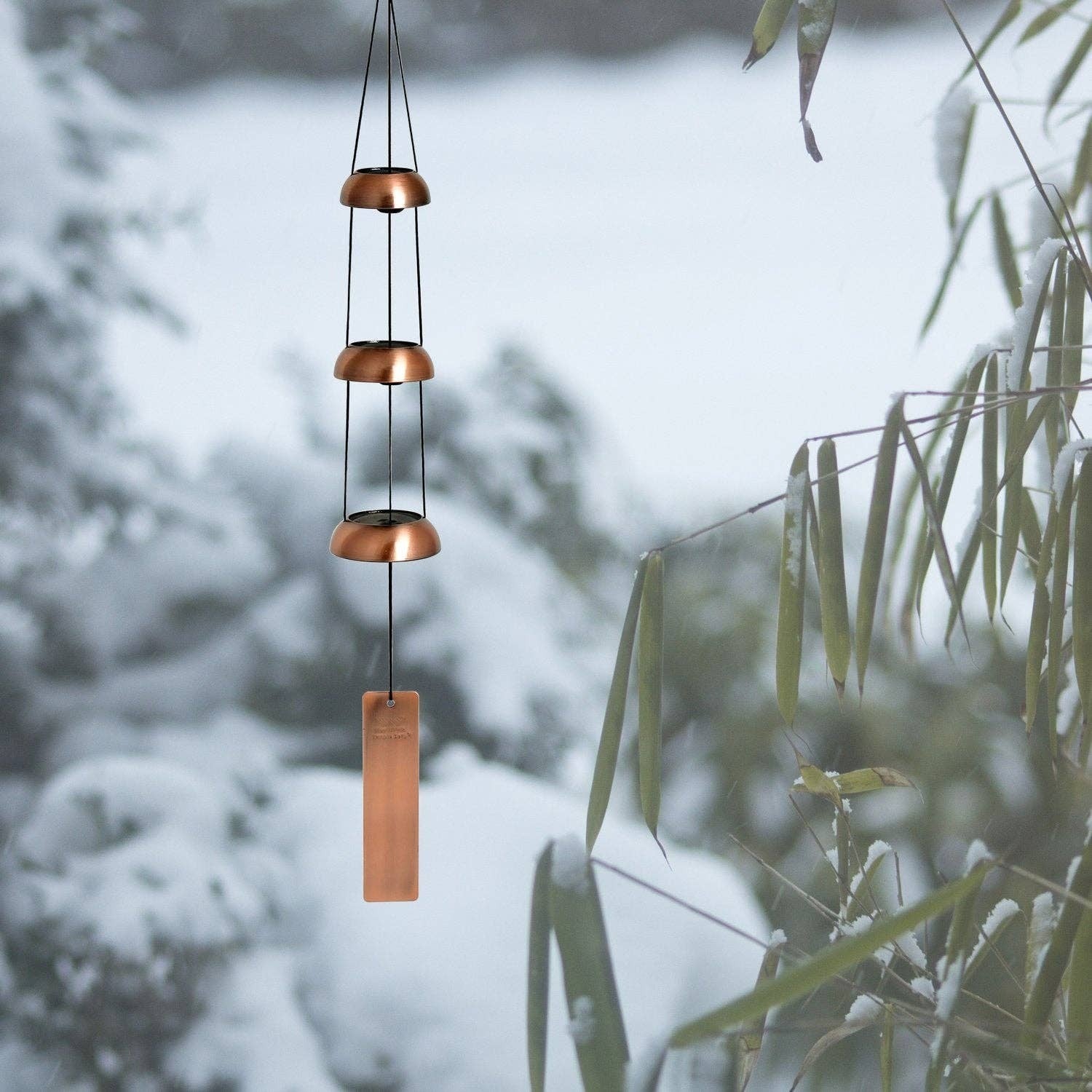 Mellow Monkey tiered copper wind chime with three bells and a rectangular wind catcher hanging in a snowy garden.