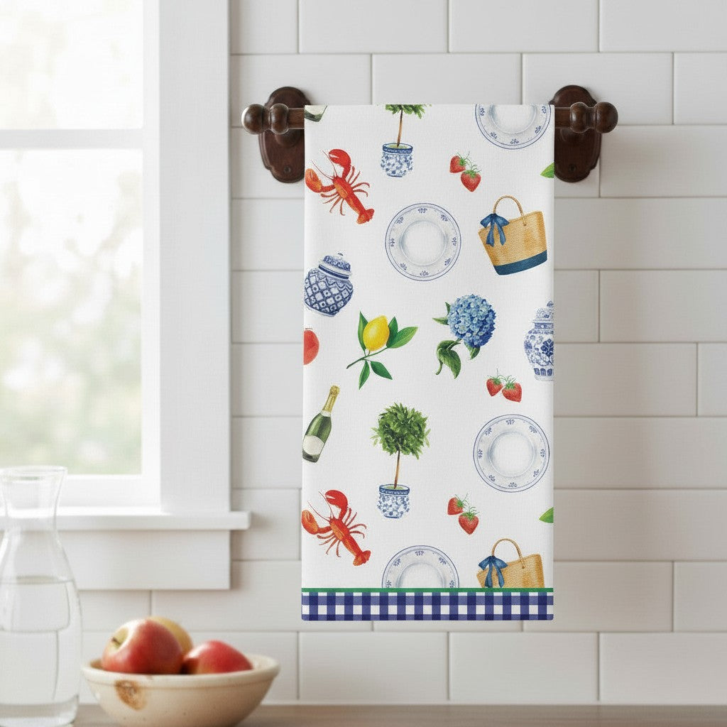 Mellow Monkey 100% cotton tea towel with a white background and a pattern of lobsters, lemons, hydrangeas, strawberries, ginger jars, and tote bags. Features a blue gingham border.