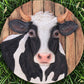 Mellow Monkey cow stepping stone and wall plaque featuring a black and white cow portrait on a rustic wood background.