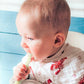 Mellow Monkey 2-in-1 baby bib and burp cloth in white muslin with red crawfish print worn by a baby in a high chair