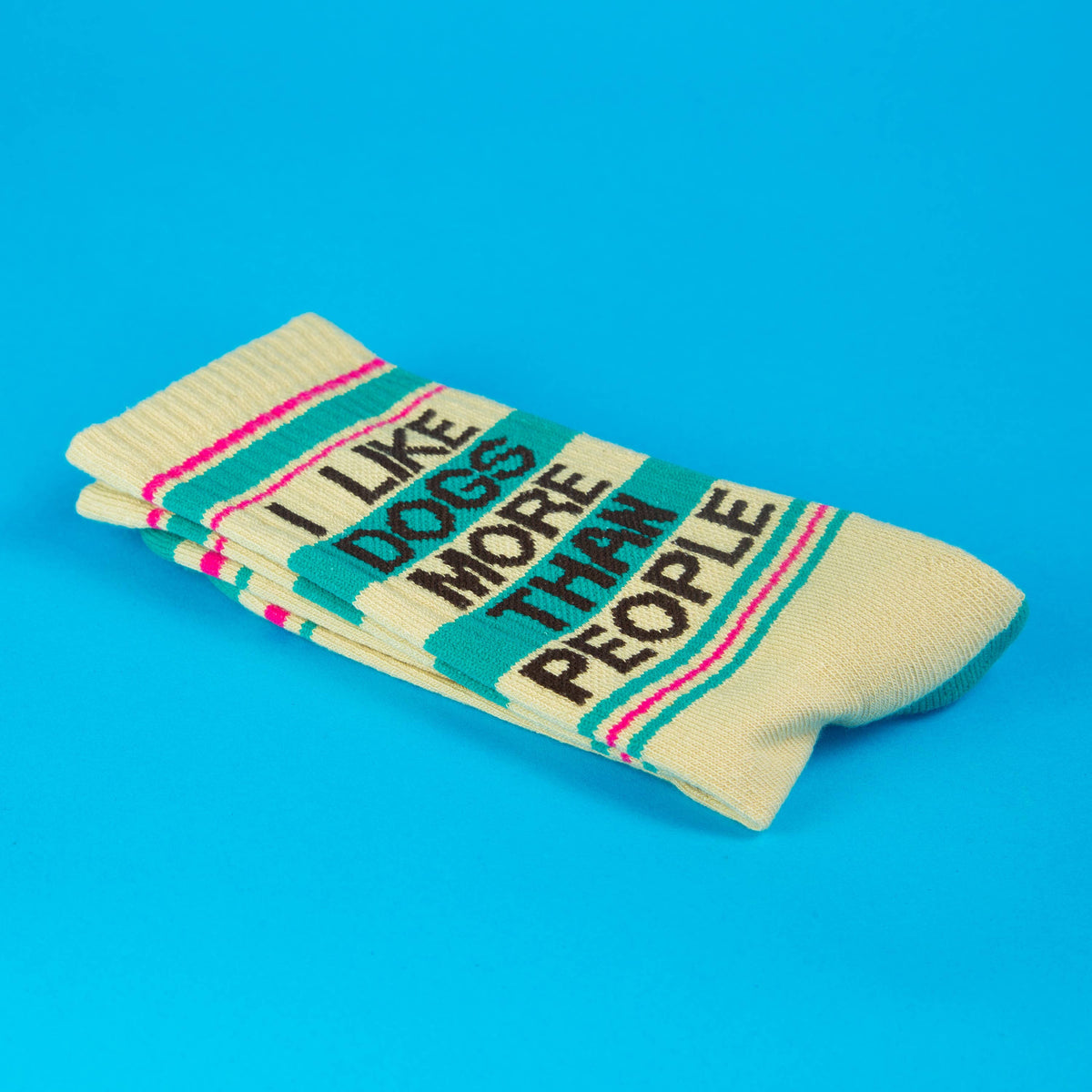 Mellow Monkey crew socks in cream with teal text reading I Like Dogs More Than People and pink striped accents.